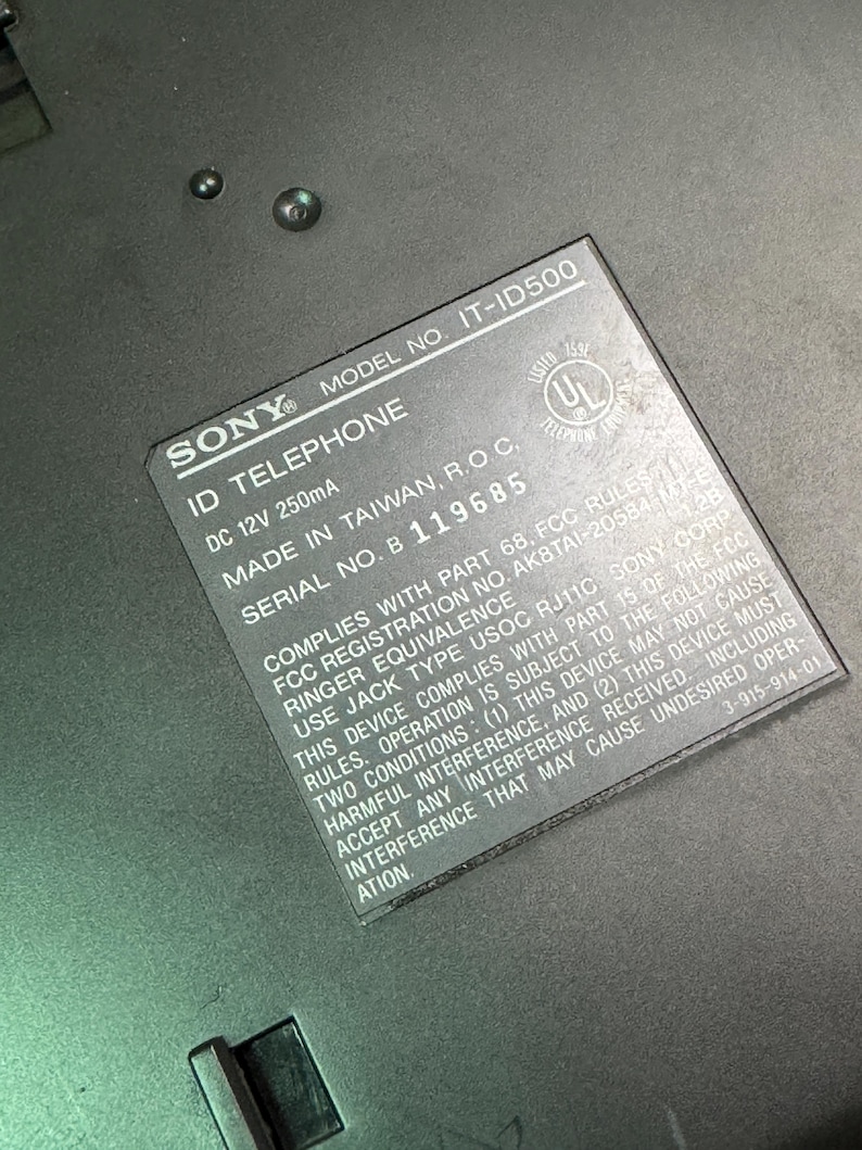 Puede incluir: Primer plano de un tel&eacute;fono ID Sony negro. La etiqueta muestra el n&uacute;mero de modelo IT-ID500, DC 12V 250mA y el n&uacute;mero de serie B 119685. La etiqueta tambi&eacute;n incluye el texto "MADE IN TAIWAN, R.O.C."