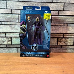 May include: A DC Multiverse action figure of Spoiler in a black and purple costume, with a yellow price tag. The figure is in a box with the DC logo and the words "SPOILER" and "COLLECT & CONNECT".