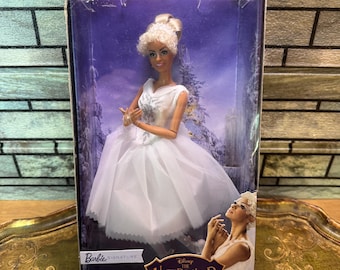 May include: A Barbie Signature doll from Disney's The Nutcracker and the Four Realms. The doll is a ballerina in a white dress with a tulle skirt, and is in a clear plastic box. The box has a winter scene background.