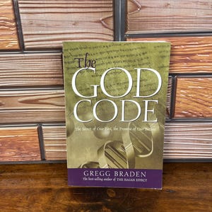 May include: A paperback book titled The God Code by Gregg Braden with a green cover featuring a DNA helix graphic and the subtitle The Secret of Our Past, the Promise of Our Future. The author is also noted as the best-selling author of The Isaiah Effect.