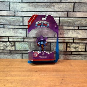 May include: A Skylanders Trap Team Blastermind action figure in a purple and clear plastic package. The figure is blue, purple, and orange. The packaging has the Skylanders logo and the text "Trap Master".