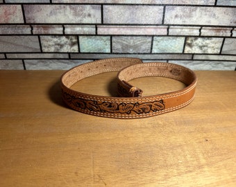 May include: A brown leather belt with a floral design. The belt is rolled up and has a stitched edge.