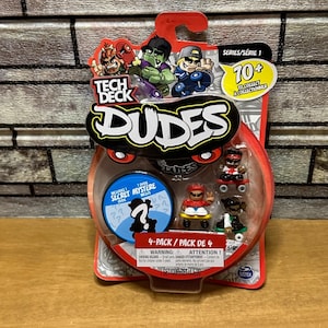 Puede incluir: Un paquete de 4 Tech Deck Dudes en un embalaje de plástico rojo y transparente. El paquete presenta personajes de monopatín de dibujos animados y el texto "Dudes". El set incluye cuatro pequeñas figuras de patinadores y una figura misteriosa.
