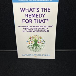 May include: A white book with a green tree illustration on the cover. The title is "What's the Remedy for That?" The subtitle is "The Definitive Homeopathy Guide to Mastering Everyday Self-Care Without Drugs". The author is Kathleen K. Fry, MD, CTHHOM.
