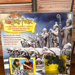 May include: A Harry Potter Wizard Chess board game box featuring a graphic of stone-like chess pieces and a small inset photo of two children playing. The box includes the title Harry Potter Wizard Chess and a black knight chess piece visible.