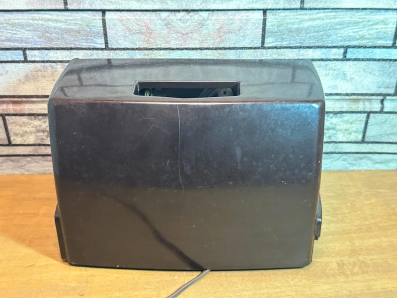 K&ouml;nnte beinhalten: Ein dunkelbraunes Vintage-Radio mit rechteckiger Form und einer kleinen rechteckigen &Ouml;ffnung oben.