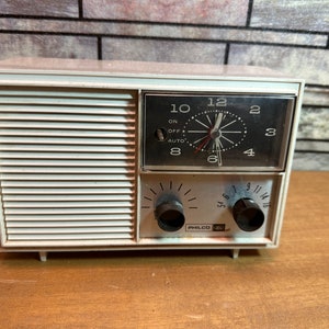 May include: A white vintage Philco AM radio with a clock and two tuning knobs. The clock face is black with white numbers and hands. The radio has a white grille with horizontal lines.