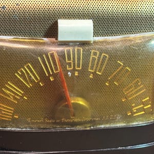 K&ouml;nnte beinhalten: Nahaufnahme eines Vintage-Radio-Zifferblatts mit einem vergilbten Kunststoffgesicht und goldenen Beschriftungen. Das Zifferblatt ist mit "Emperor Radio and Phonograph Corporation, N.Y." beschriftet.