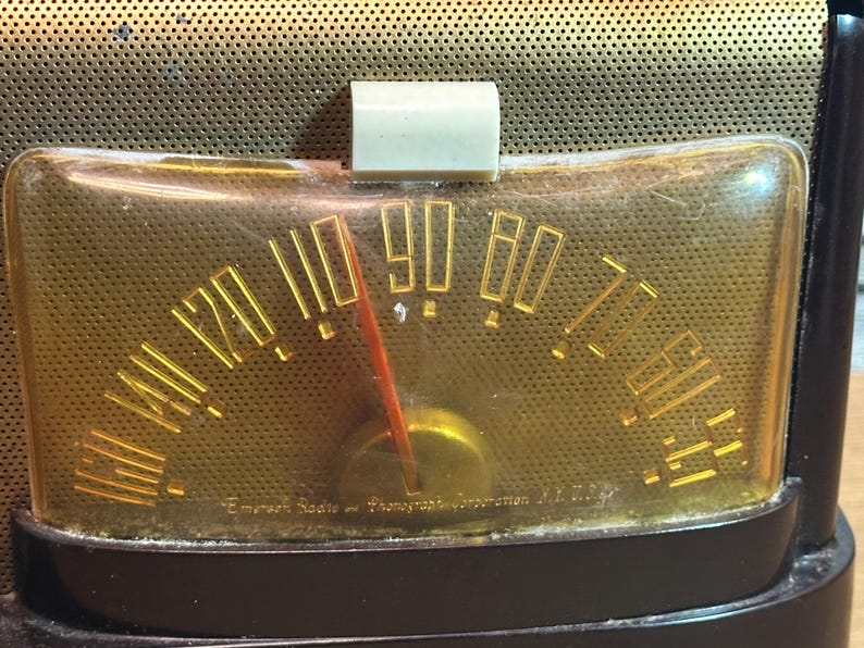 K&ouml;nnte beinhalten: Nahaufnahme eines Vintage-Radio-Zifferblatts mit einem vergilbten Kunststoffgesicht und goldenen Beschriftungen. Das Zifferblatt ist mit "Emperor Radio and Phonograph Corporation, N.Y." beschriftet.
