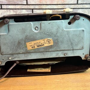K&ouml;nnte beinhalten: Ein Vintage-Radio in Braun und Schwarz mit einem Metallgitter und einem Etikett mit der Aufschrift "MODEL 511 105-125 VOLTS AC-DC 30 WATTS UL".