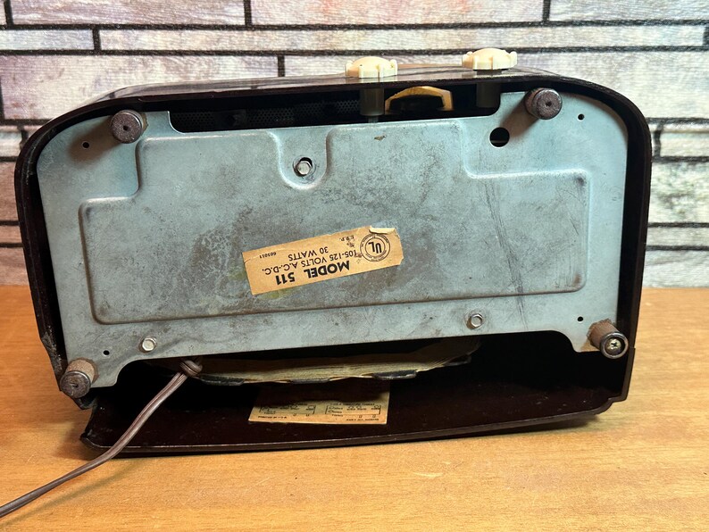 K&ouml;nnte beinhalten: Ein Vintage-Radio in Braun und Schwarz mit einem Metallgitter und einem Etikett mit der Aufschrift "MODEL 511 105-125 VOLTS AC-DC 30 WATTS UL".