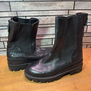 May include: A pair of black ankle boots with a textured, faux-crocodile pattern on the heel and a chunky sole. The boots have a zipper on the back and are made of a smooth, leather-like material.