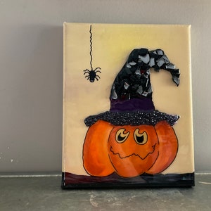 Peut inclure: Une citrouille en mosaïque avec un chapeau de sorcière noir et une araignée noire suspendue à une toile. La citrouille a un visage amical avec des détails orange, jaunes et noirs.