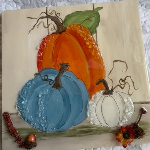 Peut inclure: Un carreau de c&eacute;ramique avec une image peinte de trois citrouilles. Les citrouilles sont orange, bleue et blanche. Le carreau a un style rustique, de ferme.