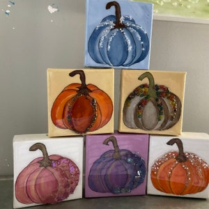 Peut inclure: Six petites toiles avec des citrouilles peintes. Chaque citrouille est d'une couleur différente, y compris le bleu, l'orange, le gris, le violet et le rose. Les citrouilles sont décorées de paillettes et de perles.