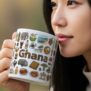 Può includere: Tazza in ceramica bianca con la scritta "Ghana" in marrone, circondata da illustrazioni colorate della cultura ghanese, tra cui un elefante, un ananas e un autobus. La tazza è tenuta in mano.