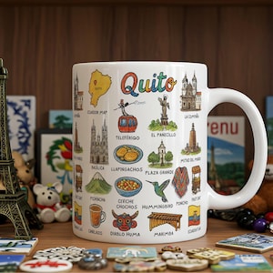 May include: White ceramic mug featuring colorful illustrations of Quito, Ecuador landmarks and cultural symbols. The word "Quito" is written in rainbow colors. The mug has a curved handle and is surrounded by decorative items.