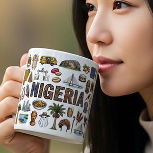 Pode incluir: Caneca de cerâmica branca com a palavra "NIGERIA" em castanho, rodeada por ilustrações coloridas de marcos e símbolos culturais nigerianos. A caneca é segurada por uma pessoa.