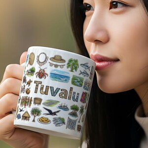 Pode incluir: Caneca de cerâmica branca com ilustrações coloridas e a palavra "Tuvalu". A caneca apresenta várias imagens, incluindo uma concha, um caranguejo, um barco e uma palmeira. A caneca é segurada por uma pessoa.