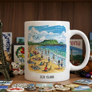 Könnte beinhalten: Weiße Keramik-Tasse mit einer Strand-Szene-Illustration, einschließlich Menschen, Sonnenschirmen und einem Berg unter blauem Himmel. Die Tasse hat einen gebogenen Griff und den Text "JEJU ISLAND".