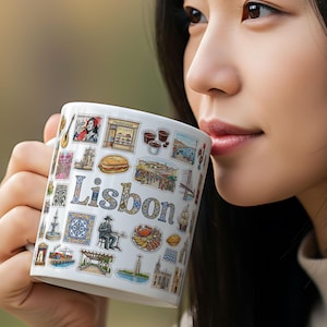 May include: White ceramic mug featuring the word "Lisbon" and various colorful illustrations of Lisbon landmarks and cultural elements. The mug is held by a person, and the design includes images of buildings, food, and other icons.