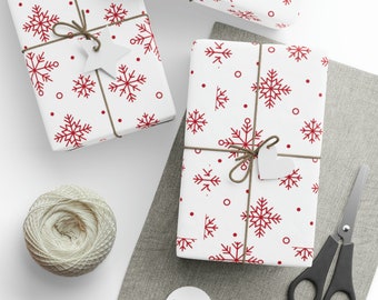 May include: White gift-wrapped boxes with a red snowflake design. The boxes are tied with twine and white tags. A ball of twine, scissors, and blank tags are also present, suggesting a festive theme.