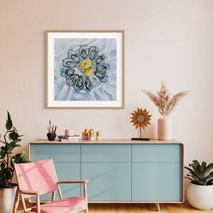 May include: A watercolor painting of a plate of oysters with lemon wedges. The oysters are arranged in a circle on a white plate with a blue background. The painting is framed in a light wood frame and hangs on a light pink wall.