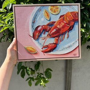 Puede incluir: Una pintura de una langosta roja en un plato azul y blanco con rodajas de limón sobre un fondo rosa.