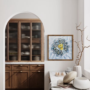 May include: A framed watercolor painting of a plate of mussels with lemon wedges, hanging on a white wall in a kitchen. The painting is in a light wood frame.