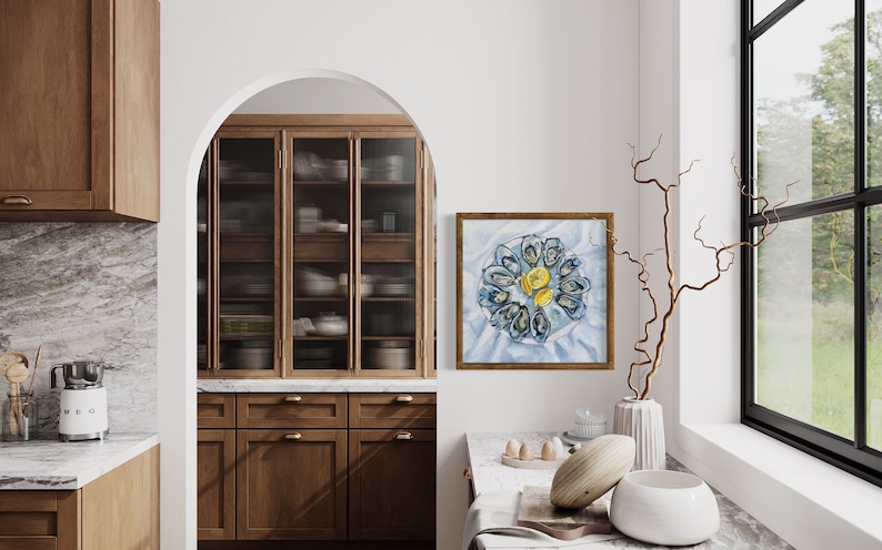 May include: A framed watercolor painting of a plate of mussels with lemon wedges, hanging on a white wall in a kitchen. The painting is in a light wood frame.