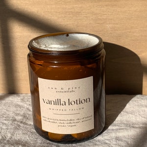 Puede incluir: Un tarro de vidrio marr&oacute;n con una etiqueta blanca que dice "sun & pine essentials Vanilla lotion WHIPPED TALLOW 100% grass fed & finished tallow, olive oil infused with calendula, whole vanilla beans, arrowroot powder. "organic"