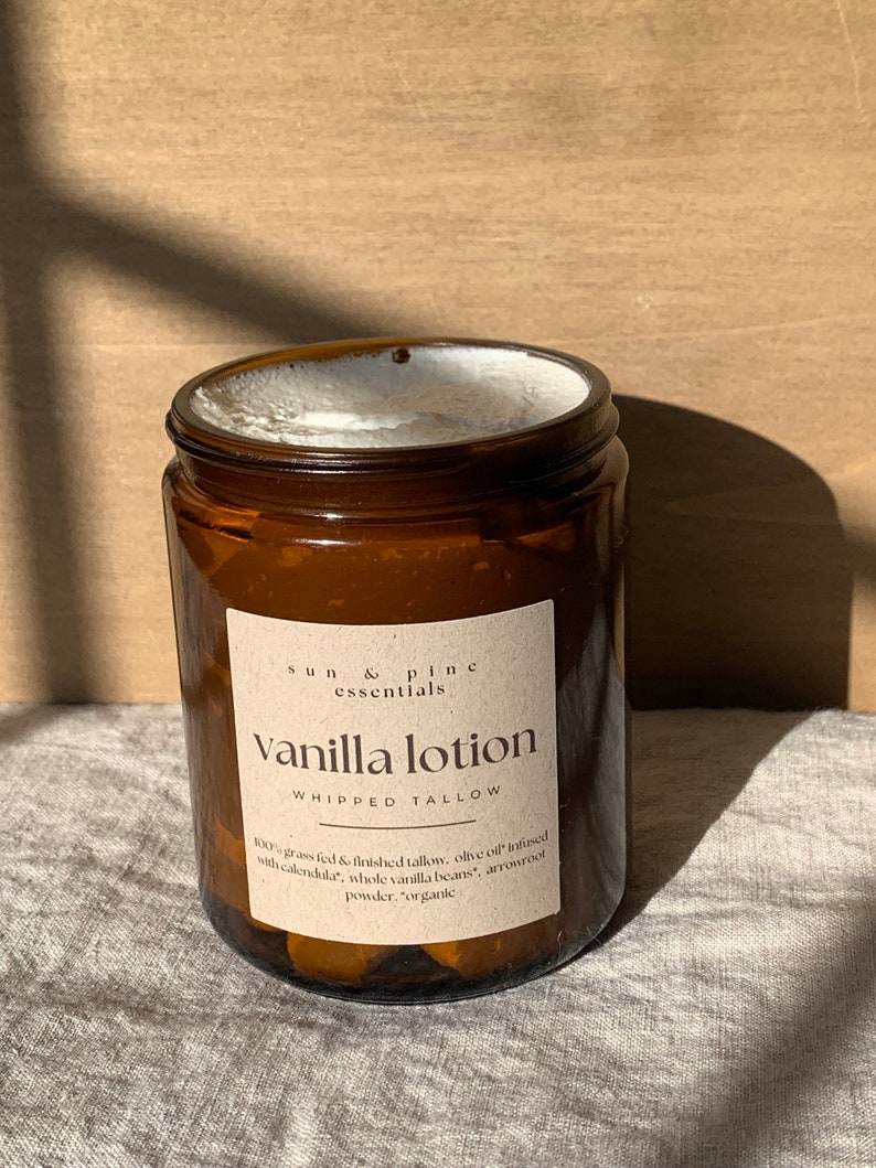 Puede incluir: Un tarro de vidrio marr&oacute;n con una etiqueta blanca que dice "sun & pine essentials Vanilla lotion WHIPPED TALLOW 100% grass fed & finished tallow, olive oil infused with calendula, whole vanilla beans, arrowroot powder. "organic"