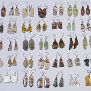 Puede incluir: Una colección de 40 pares de pendientes de plata con diferentes formas y colores de piedra. Las piedras son todas naturales y tienen un patrón único. Los pendientes son perfectos para añadir un toque de elegancia a cualquier atuendo.