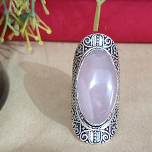 May include: A silver ring with an oval-shaped pink stone set in an ornate silver setting.