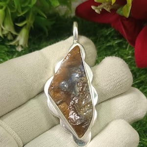 May include: A silver pendant with a brown and blue opal stone. The pendant has a scalloped edge and a bail for attaching a chain.