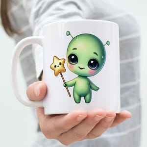 Puede incluir: Taza de cer&aacute;mica blanca con un extraterrestre verde sosteniendo una varita de estrella amarilla. El extraterrestre tiene ojos grandes y una sonrisa linda.
