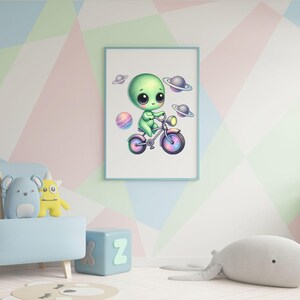 Puede incluir: Un extraterrestre verde con ojos grandes montando una bicicleta rosa y azul con ruedas de arco&iacute;ris. El extraterrestre est&aacute; rodeado de peque&ntilde;os planetas sobre un fondo blanco.