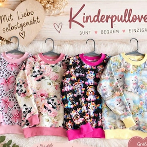 Könnte beinhalten: Vier langärmelige Pullover an grauen Kleiderbügeln. Der erste hat ein rosa Leoparden- und Schleifenmuster, der zweite zeigt Pandas und rosa Blumen, der dritte bunte Einhörner auf Schwarz und der vierte weiße Kätzchen mit Blumen.