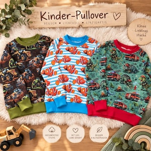 Könnte beinhalten: Drei langärmelige Pullover für Kinder. Der linke Pullover ist braun mit gelben Baustellenfahrzeugen und olivgrünen Bündchen. Der mittlere Pullover zeigt orangefarbene Clownfische auf blauen Streifen. Der rechte Pullover ist grün mit roten Feuerwehrautos, Dinosauriern und roten Bündchen.
