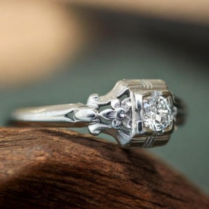 May include: A silver engagement ring with a single round diamond set in a delicate floral design.