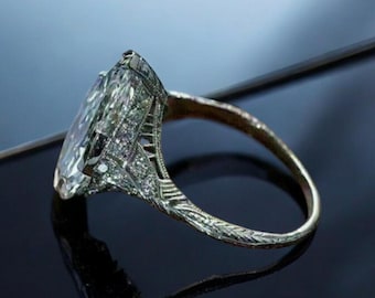 May include: A silver ring with a large, clear, oval-shaped gemstone surrounded by smaller diamonds. The ring has an intricate, filigree design.