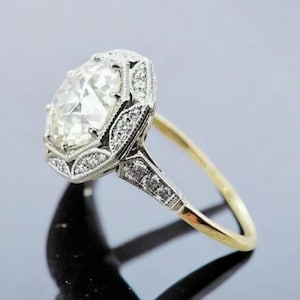 May include: A vintage-style engagement ring featuring a large, round, clear diamond set in a platinum setting. The ring has a delicate, filigree design and is accented with smaller diamonds. The band is made of yellow gold.