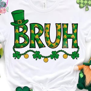 Op de afbeelding: Wit T-shirt met het woord "BRUH" in groen en geel, versierd met klavers en een groene hoge hoed. Een klaverblad slinger met gouden munten staat onder het woord. Het shirt is omgeven door decoraties met het thema St. Patrick's Day.