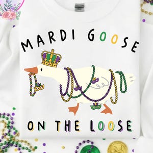 May include: White sweatshirt featuring a goose wearing a crown and Mardi Gras beads. The text "MARDI GOOSE ON THE LOOSE" is printed above and below the goose illustration. The sweatshirt has a crew neck.