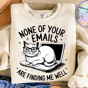 以下が含まれることがあります： 眼鏡をかけた猫がラップトップに座っている白黒のイラストが描かれた白いスウェットシャツ。スウェットシャツには「None of your emails are finding me well」というテキストが印刷されています。