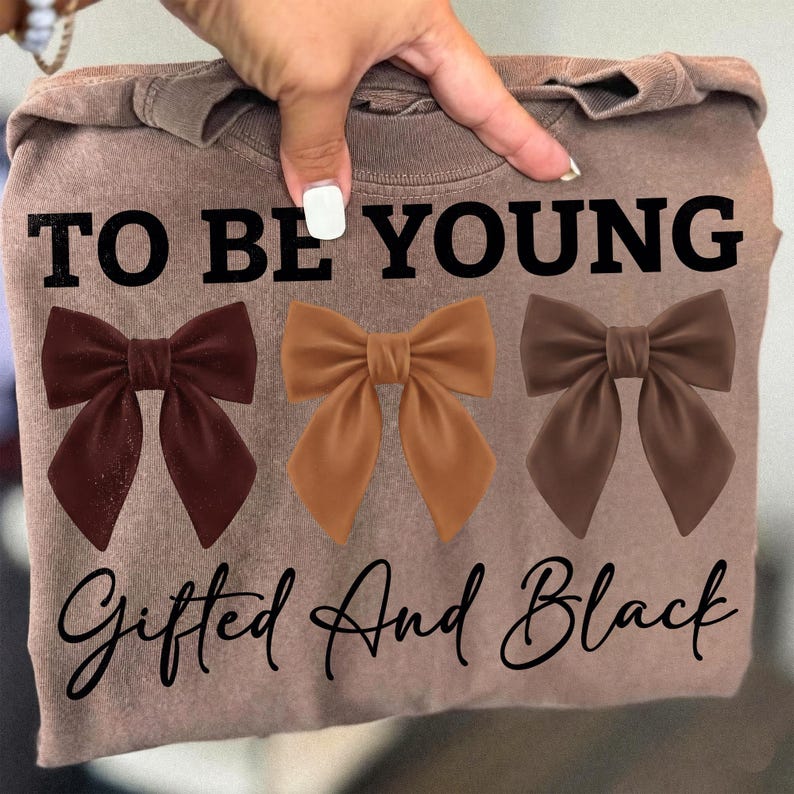 Op de afbeelding: Een bruine sweatshirt met de tekst "TO BE YOUNG" boven drie strik-afbeeldingen in bruin- en beigetinten. Onder de strikken staat de tekst "Gifted And Black".