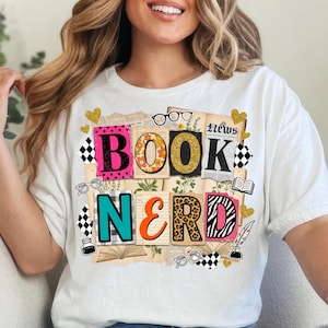 May include: White t-shirt with a colourful "Book Nerd" graphic. The design features the words "BOOK" and "NERD" in various fonts and patterns, including leopard print and floral elements, with glasses and hearts.