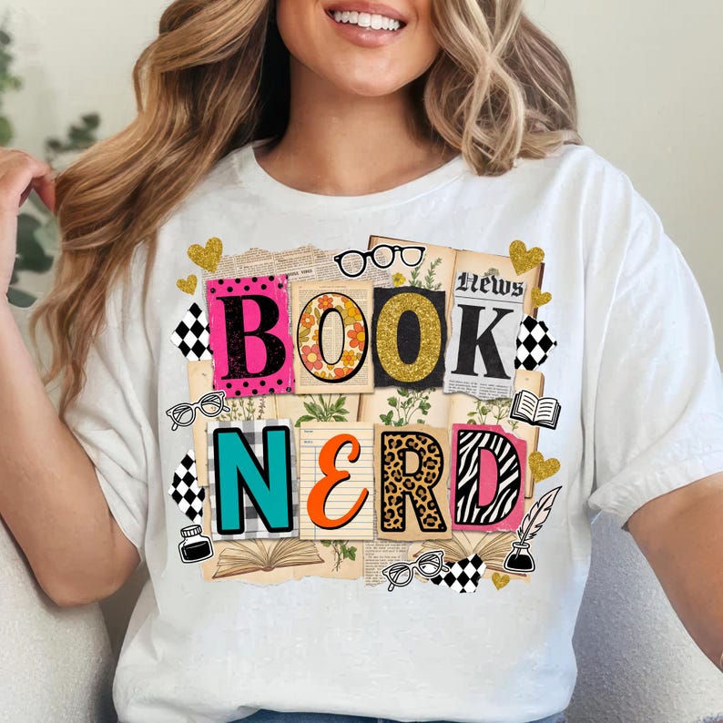 May include: White t-shirt with a colourful "Book Nerd" graphic. The design features the words "BOOK" and "NERD" in various fonts and patterns, including leopard print and floral elements, with glasses and hearts.