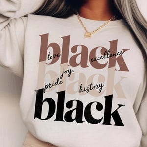 May include: A white sweatshirt with the words "black" in black, brown, and beige lettering. The words "love", "joy", "pride", "excellence", "history" are written in black cursive lettering around the word "black".
