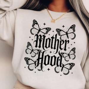 Puede incluir: Sudadera color crema con un dise&ntilde;o de mariposas y estrellas negras. Las palabras "Mother Hood" est&aacute;n escritas en una fuente g&oacute;tica. El dise&ntilde;o incluye seis mariposas y peque&ntilde;os acentos de estrellas.